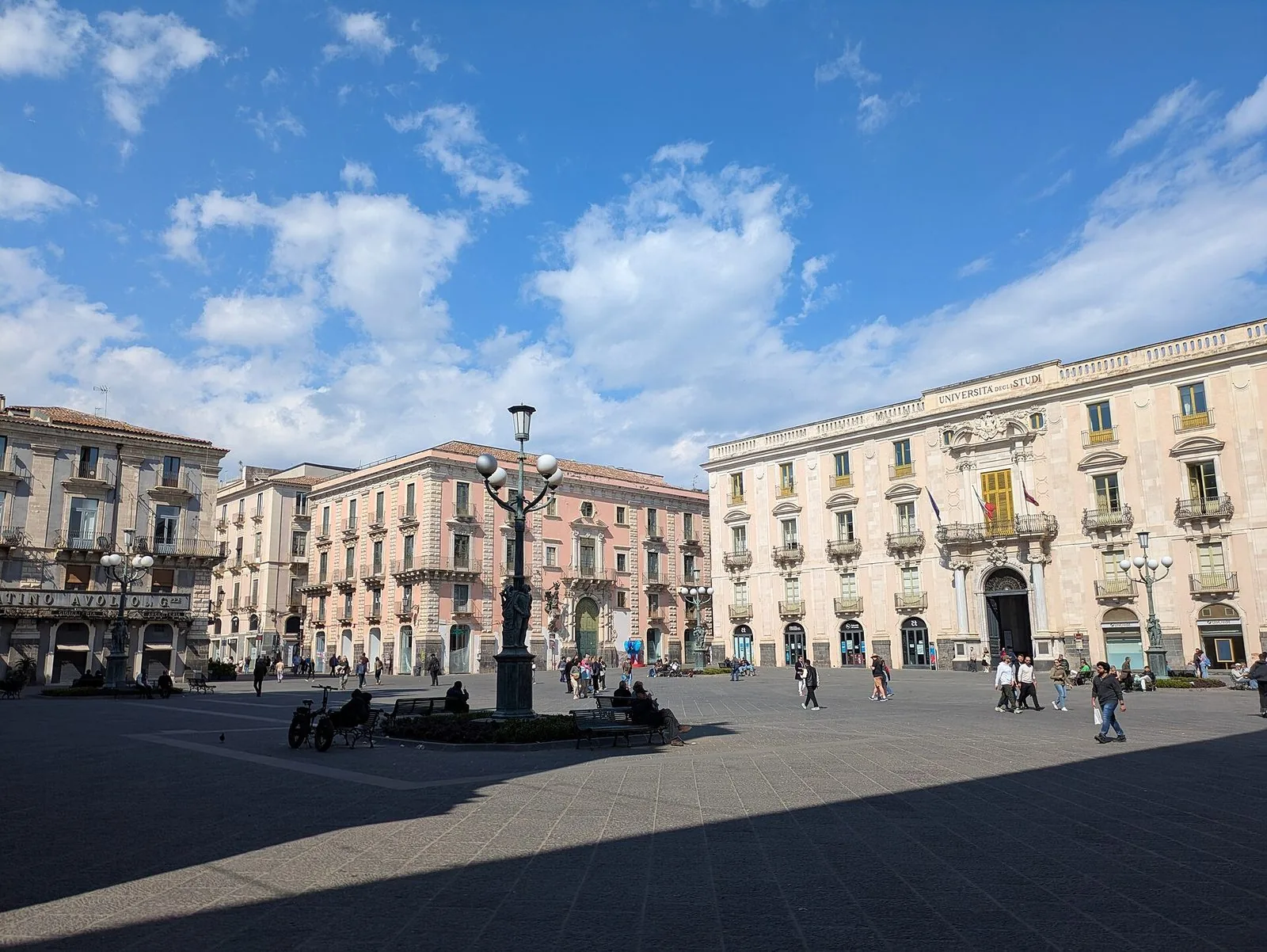 Piazza Università a Catania con il Palazzo dell'Università, un candelabro in bronzo e i palazzi barocchi sotto un cielo azzurro