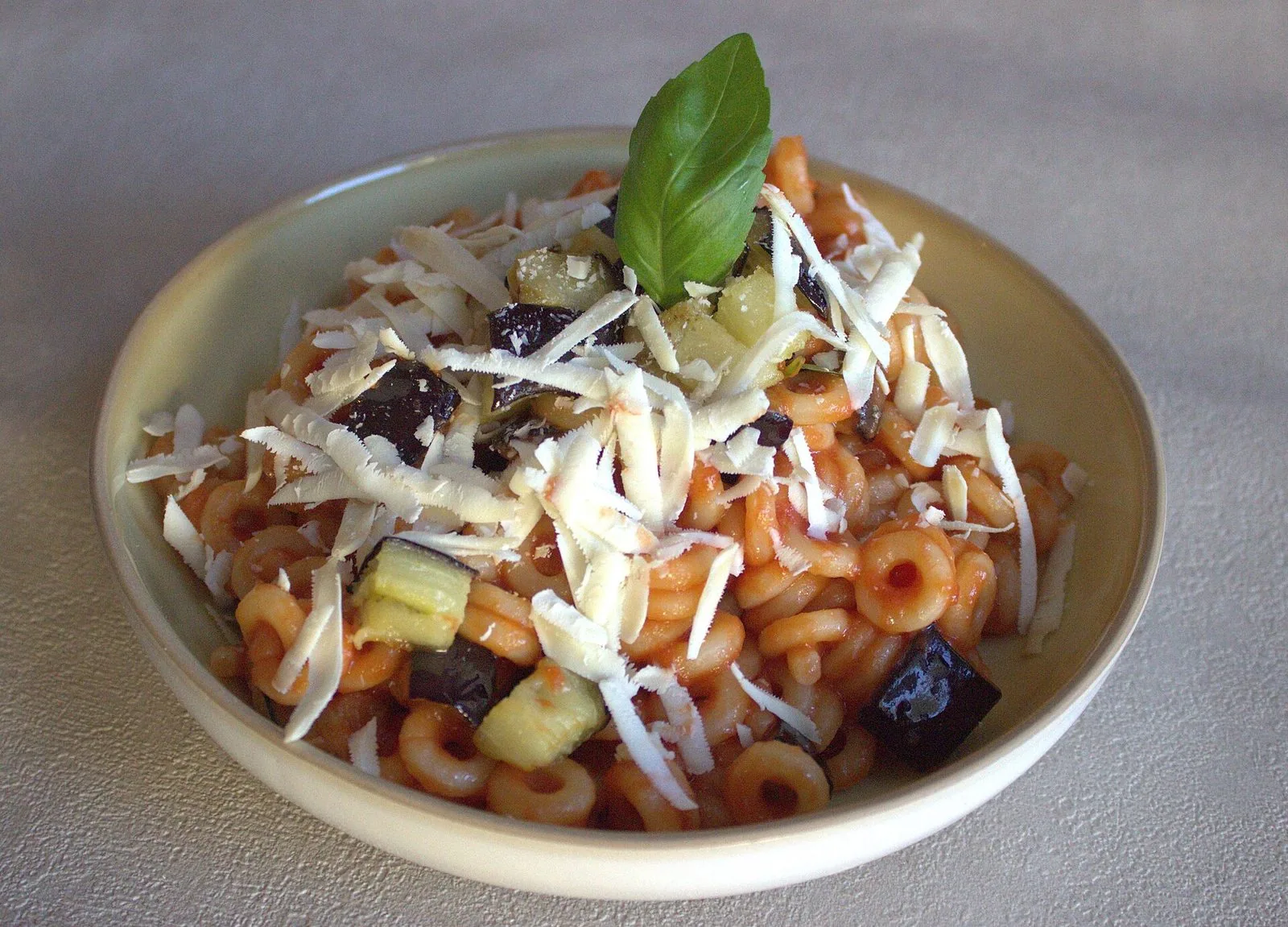 Un piatto di pasta alla Norma con salsa di pomodoro, melanzane fritte, ricotta salata grattugiata e una foglia di basilico