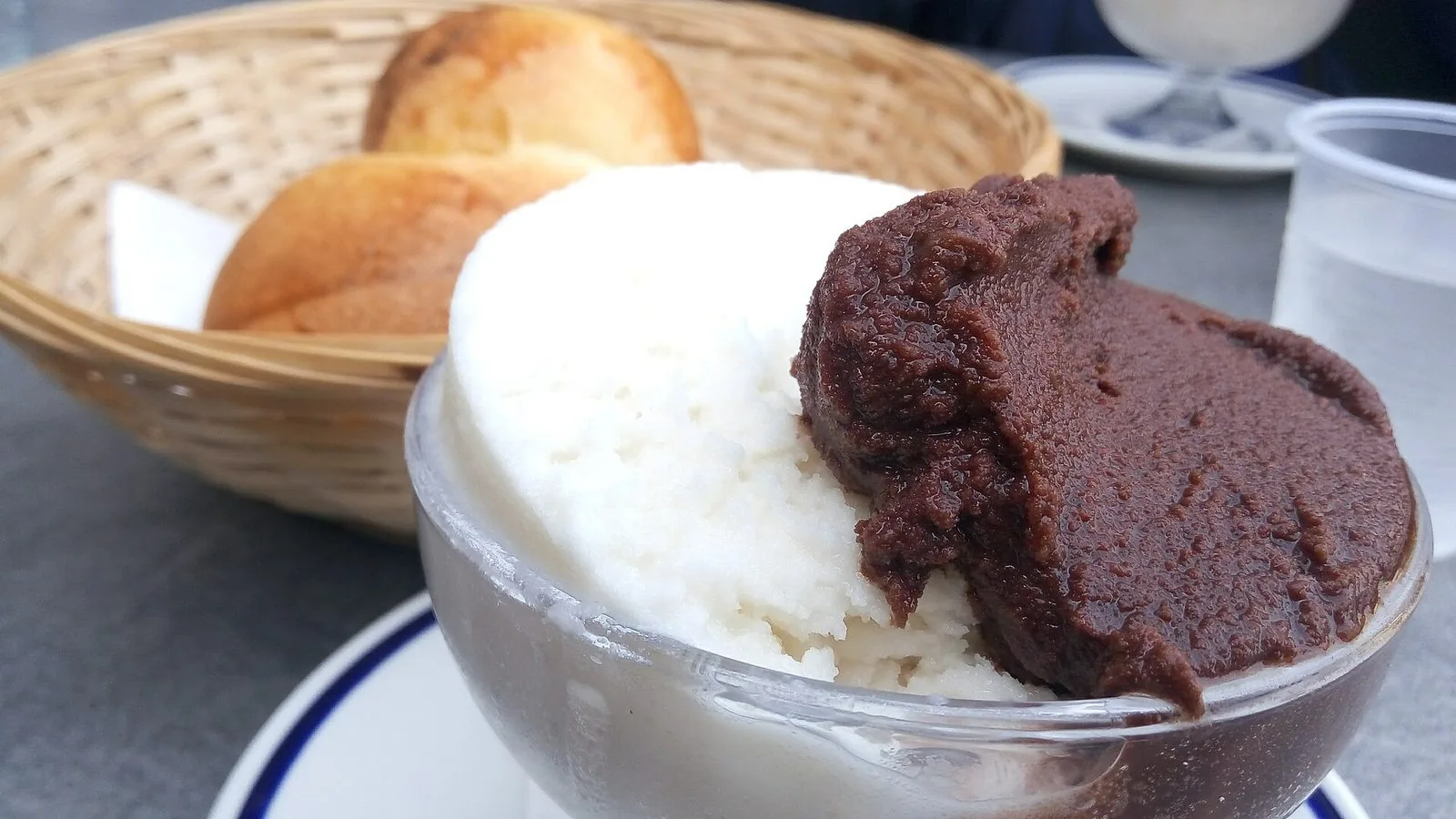 Coppa di granita siciliana ai gusti mandorla e cioccolato con un cestino di brioche sullo sfondo